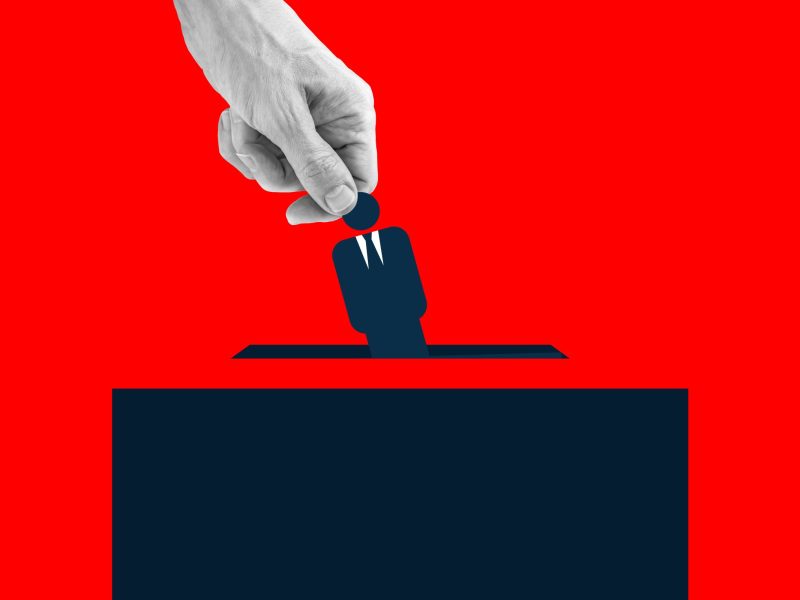 Human hand placing an icon of man wearing suit into the voting box. Via Getty Images
