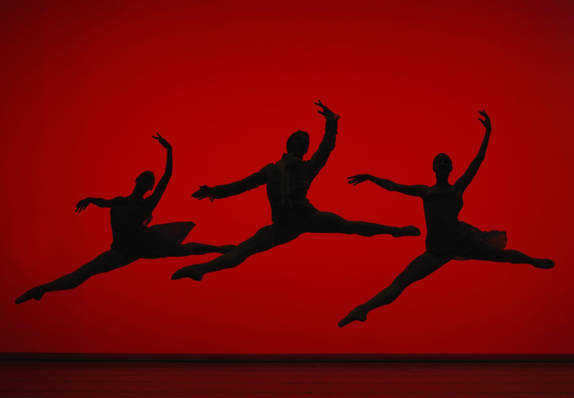 Three ballet dancers leaping on stage, silhouette