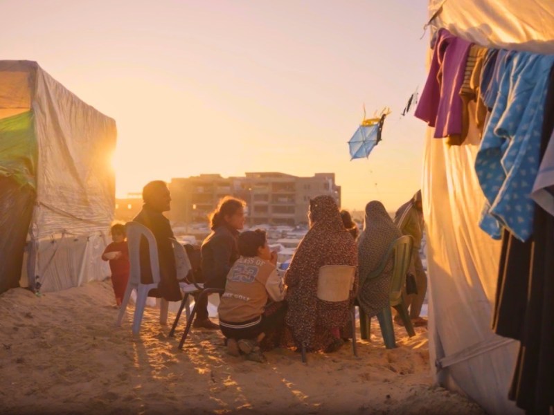 A family in Gaza shares a brief moment together at sunset outside of their tent in a makeshift refugee camp. Screenshot from video by Ruwaida Amer
